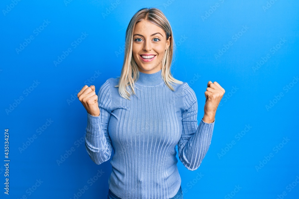 Beautiful blonde woman wearing casual clothes celebrating surprised and amazed for success with arms raised and open eyes. winner concept. Beautiful blonde woman wearing casual clothes celebrating surprised and amazed for success with arms raised and open eyes. winner concept.