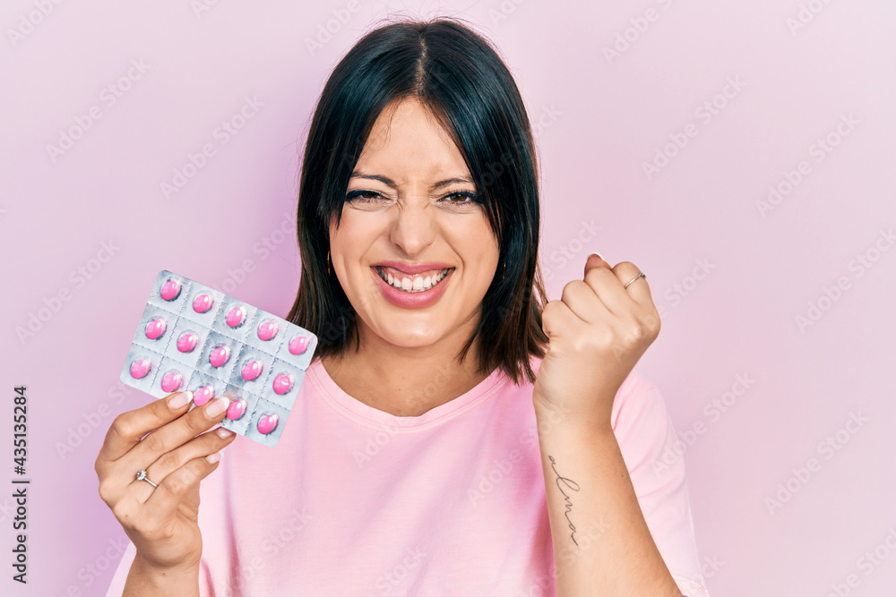 Young hispanic woman holding pills screaming proud, celebrating victory and success very excited with raised arms Young hispanic woman holding pills screaming proud, celebrating victory and success very excited with raised arms