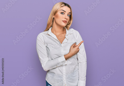 Young caucasian woman wearing casual clothes pointing with hand finger to the side showing advertisement, serious and calm face