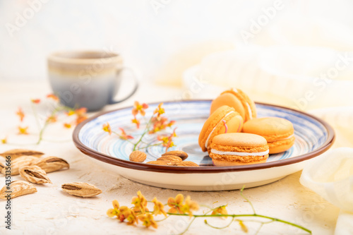 Orange macarons or macaroons cakes with cup of coffee on a white concrete background. Side view, selective focus.