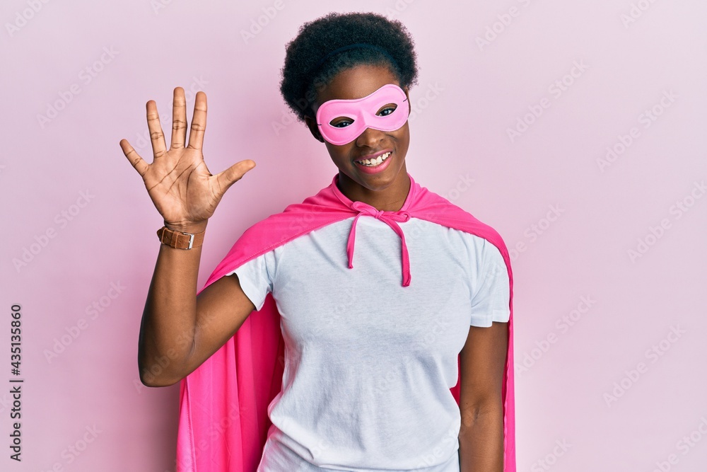 Young african american girl wearing superhero mask and cape costume showing and pointing up with fingers number five while smiling confident and happy. Young african american girl wearing superhero mask and cape costume showing and pointing up with fingers number five while smiling confident and happy.