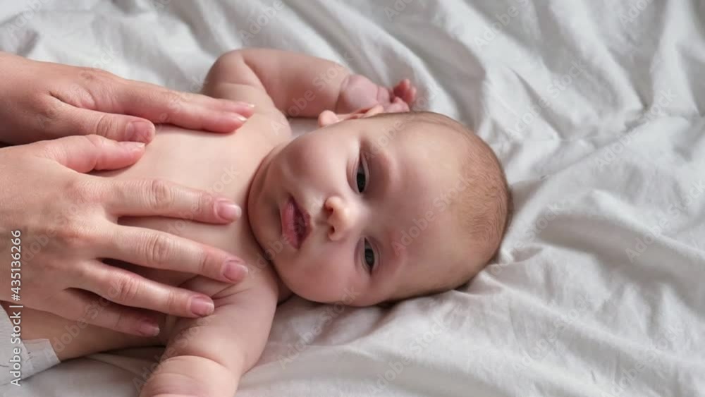Mother massaging little baby. Newborn Baby skin care concept. Prevention of colic. Female hands doing massage to newborn. Slow motion. Nice caucasian infant baby lying at the back. Portrait. Close up. Mother massaging little baby. Newborn Baby skin care concept. Prevention of colic. Female hands doing massage to newborn. Slow motion. Nice caucasian infant baby lying at the back. Portrait. Close up.