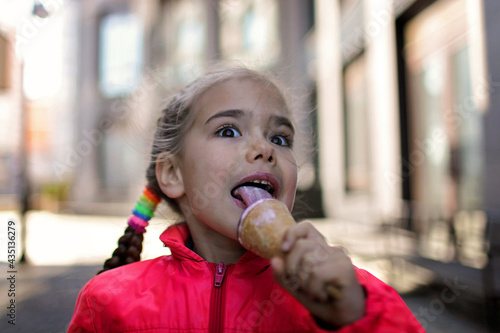Pretty little girl in pink coat eating an ice-cream in the city street, spring outdoor lifestyle