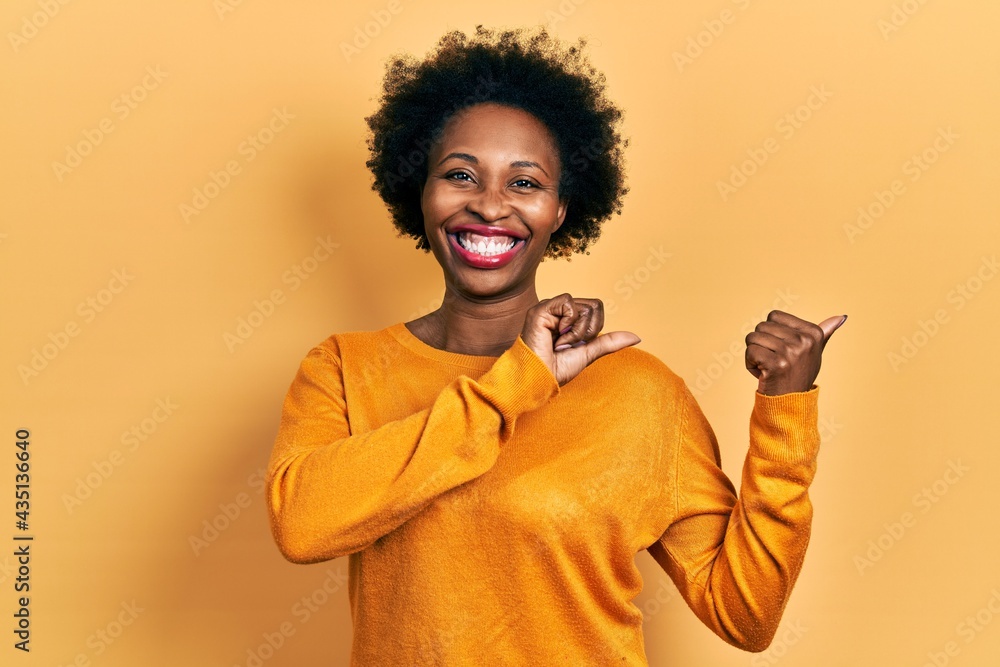 Young african american woman wearing casual clothes pointing to the back behind with hand and thumbs up, smiling confident Young african american woman wearing casual clothes pointing to the back behind with hand and thumbs up, smiling confident