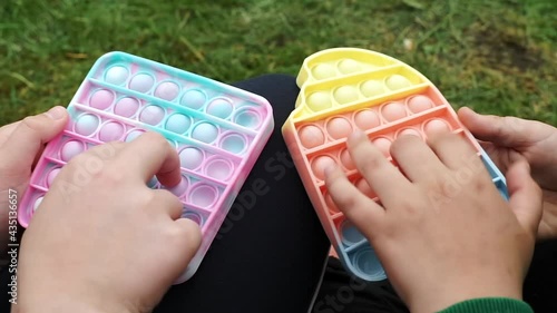 Anonymous children Siblings playing with colorful poppit sensory game. Close up of kid hands Push colorful trendy pop bubble flexible fidget toy. Concentration, antistress, mental issues concept..