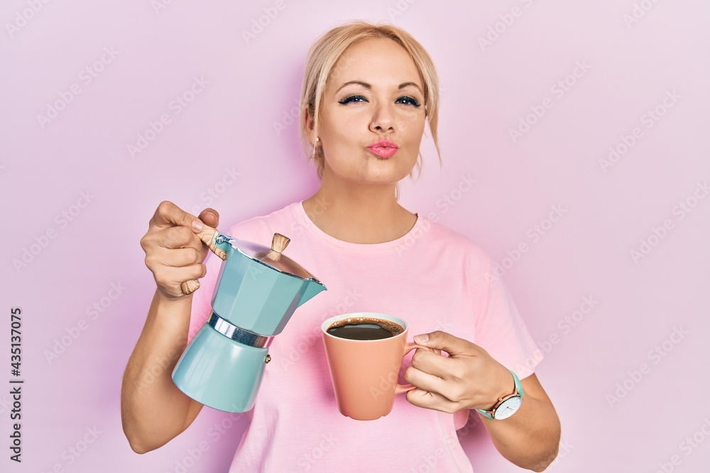 Young blonde woman drinking a cup fresh coffee looking at the camera blowing a kiss being lovely and sexy. love expression. Young blonde woman drinking a cup fresh coffee looking at the camera blowing a kiss being lovely and sexy. love expression.