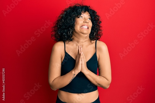 Young hispanic woman wearing casual style with sleeveless shirt begging and praying with hands together with hope expression on face very emotional and worried. begging.
