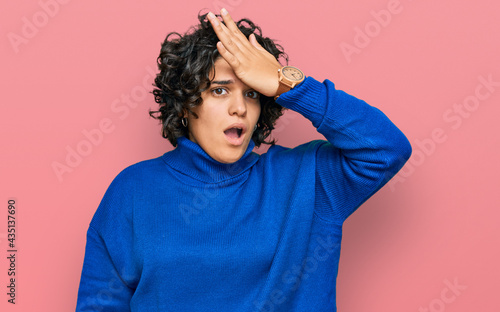 Young hispanic woman with curly hair wearing turtleneck sweater surprised with hand on head for mistake, remember error. forgot, bad memory concept. © Krakenimages.com