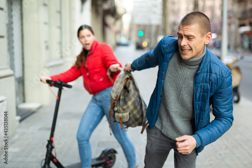 Male thief stealing bagback from scared woman on street