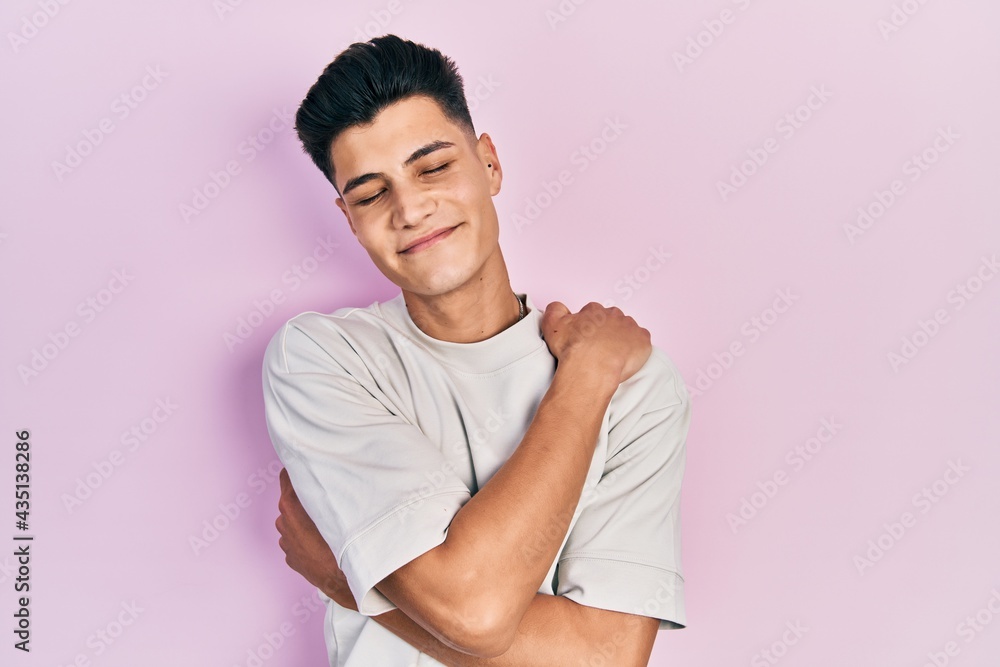 Young hispanic man wearing casual white t shirt hugging oneself happy and positive, smiling confident. self love and self care Young hispanic man wearing casual white t shirt hugging oneself happy and positive, smiling confident. self love and self care