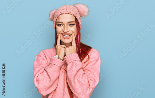 Young caucasian woman wearing casual clothes and wool cap smiling with open mouth, fingers pointing and forcing cheerful smile