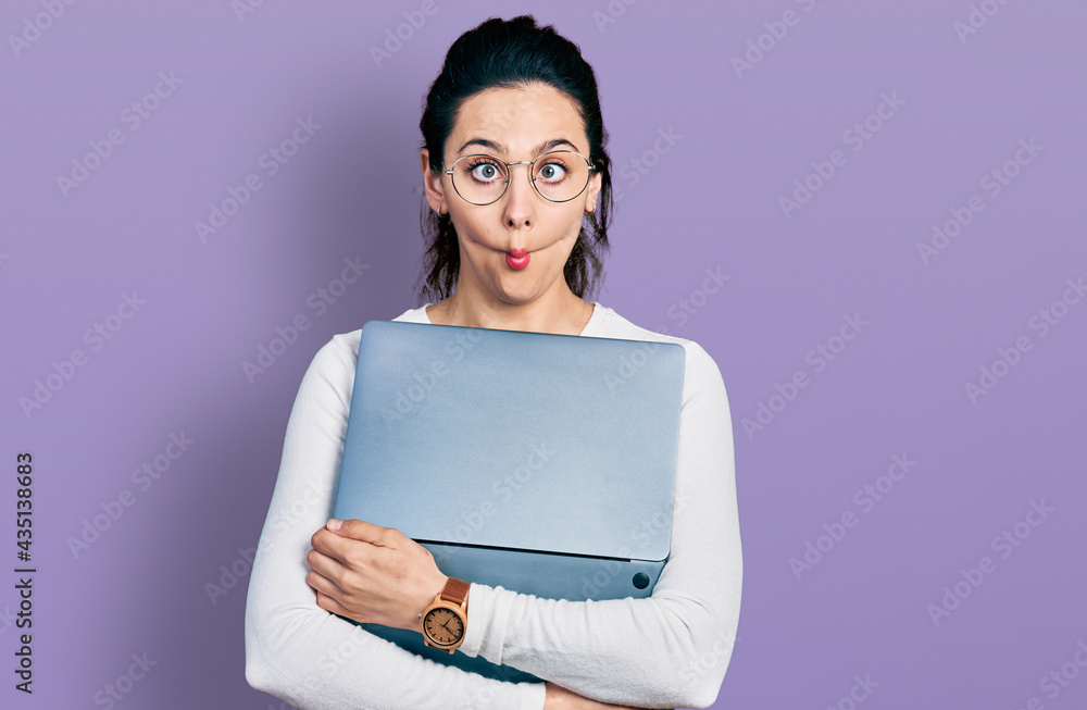Young hispanic woman working using computer laptop making fish face with mouth and squinting eyes, crazy and comical. Young hispanic woman working using computer laptop making fish face with mouth and squinting eyes, crazy and comical.