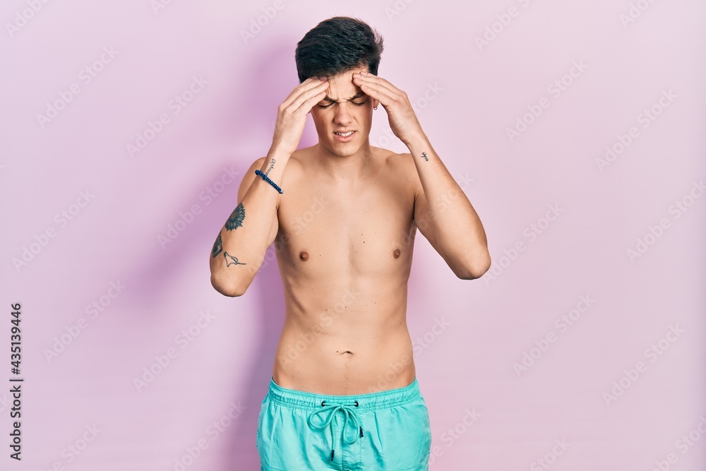Fototapeta premium Young hispanic man wearing swimwear shirtless with hand on head for pain in head because stress. suffering migraine.