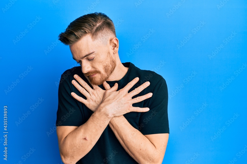 Young redhead man wearing casual black t shirt hugging oneself happy and positive, smiling confident. self love and self care Young redhead man wearing casual black t shirt hugging oneself happy and positive, smiling confident. self love and self care