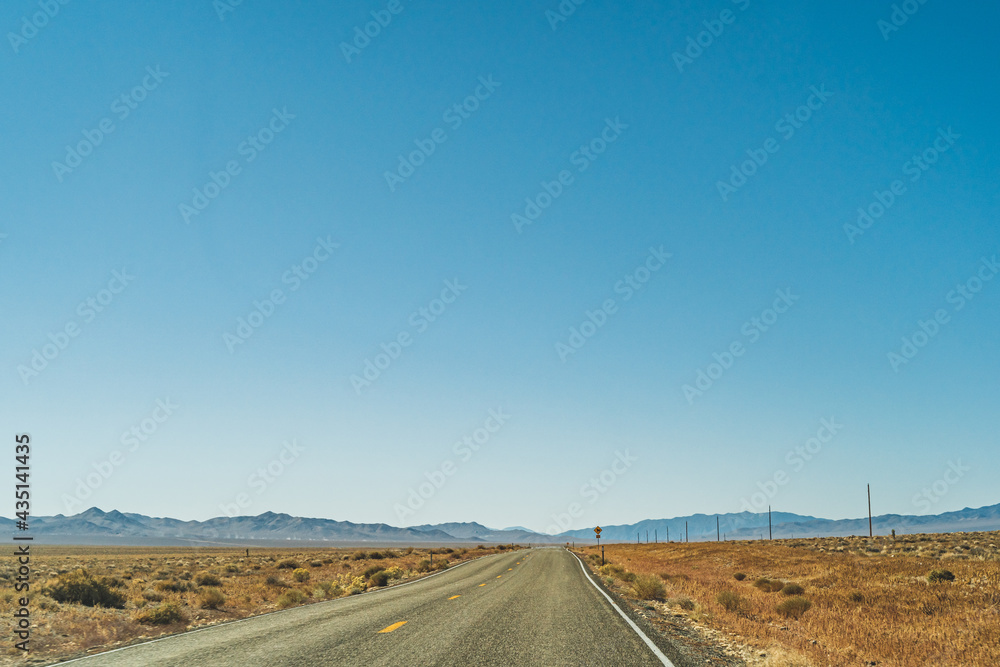 Desert highway road leading to the horizon against clear blue sky and mountains