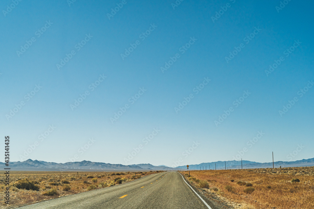 Desert highway road leading to the horizon against clear blue sky and mountains Desert highway road leading to the horizon against clear blue sky and mountains