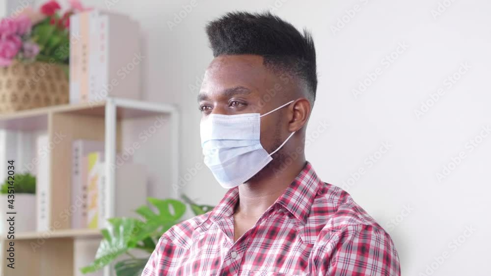 African man wearing mask sitting down on a sofa at home. Trying to protect virus and pollution. Feeling bored and fear disease. Coronavirus quarantine African man wearing mask sitting down on a sofa at home. Trying to protect virus and pollution. Feeling bored and fear disease. Coronavirus quarantine