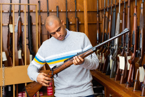 Portrait of male owner of hunting shop standing with shotgun indoors