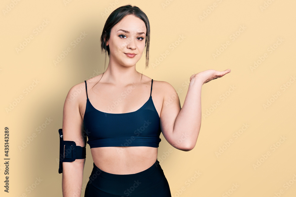 Young hispanic woman wearing sportswear smiling cheerful presenting and pointing with palm of hand looking at the camera. Young hispanic woman wearing sportswear smiling cheerful presenting and pointing with palm of hand looking at the camera.