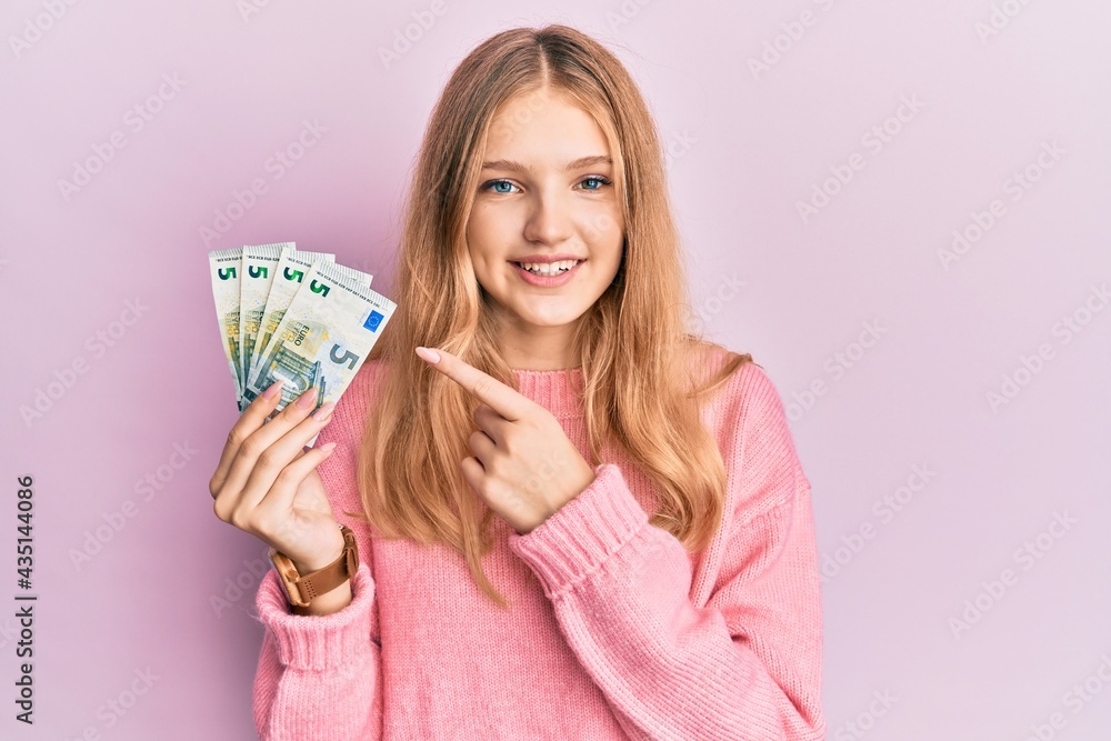 Beautiful young caucasian girl holding bunch of 5 euro banknotes smiling happy pointing with hand and finger Beautiful young caucasian girl holding bunch of 5 euro banknotes smiling happy pointing with hand and finger