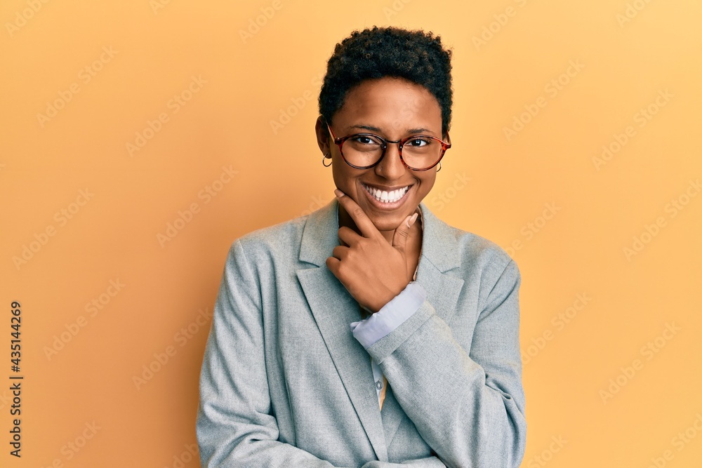 Young african american girl wearing business jacket and glasses looking confident at the camera smiling with crossed arms and hand raised on chin. thinking positive. Young african american girl wearing business jacket and glasses looking confident at the camera smiling with crossed arms and hand raised on chin. thinking positive.