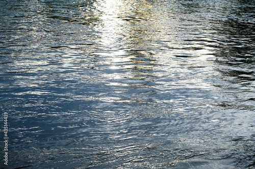Sun reflection on water surface. Disturbed river surface at sunset. 
