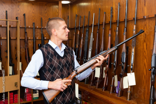 Portrait of interested man carefully choosing hunting rifle in modern gun shop .