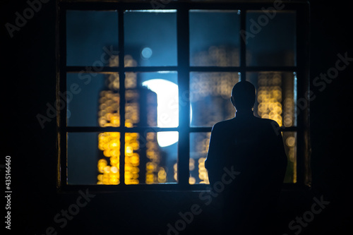 The silhouette of a man with arms crossed in front of a window with a view over a city lit in the night.