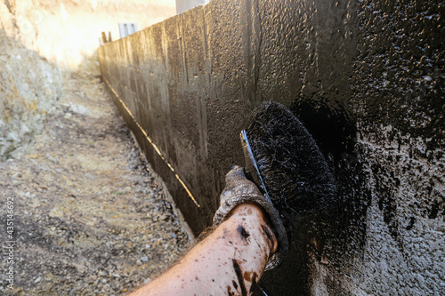 Protective waterproofing coating of walls in contact with the ground with bituminous mastic. Worker hand  applies bitumen mastic on the foundation. photo