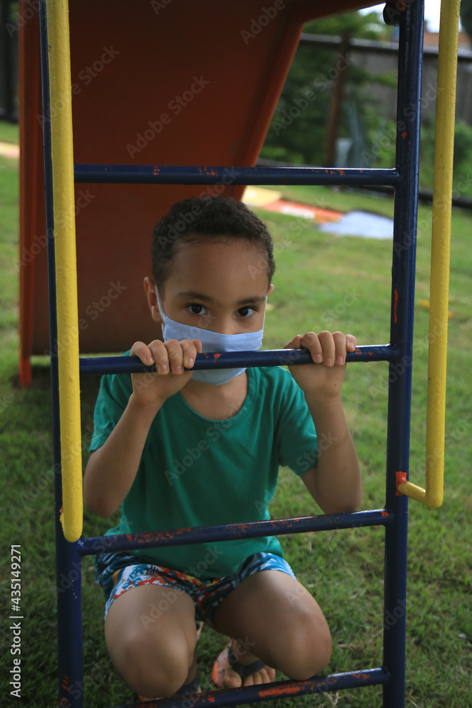 Obraz premium salvador, bahia, brazil - may 15, 2021: child plays in a playground using chewing protection against the coronavirus in the city of Salvador.