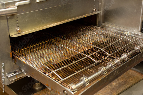 A view of a conveyor oven appliance, in a restaurant kitchen setting.