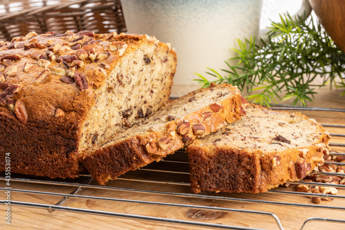 A loaf of banana bread with pecan pieces baked in fresh from the oven with a slice cut off
 photo