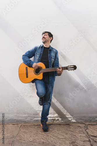 Músico contemporáneo sonriendo y cantando con su guitarra española vestido de denim