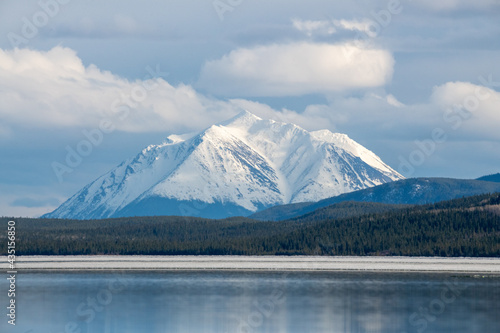 Stunning landscape of Yukon Territory in May, spring time with partially frozen lake, epic mountain peak in background and wilderness boreal forest. 