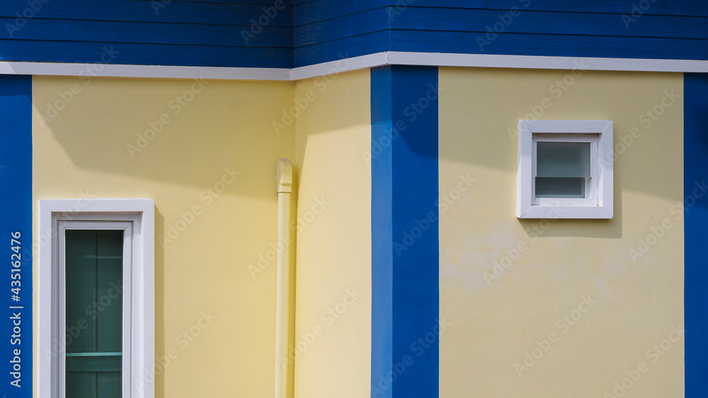 Perspective view of 2 white fixing windows with air vent pipe on yellow and blue house building wall in modern style Perspective view of 2 white fixing windows with air vent pipe on yellow and blue house building wall in modern style