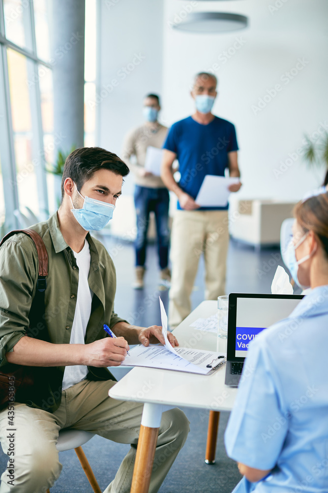 Young man talking to nurse while filling paperwork at COVID-19 vaccination center. Young man talking to nurse while filling paperwork at COVID-19 vaccination center.