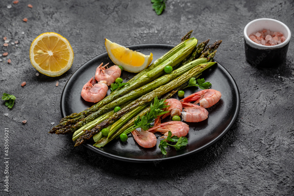Plate with a keto diet food. baked asparagus, shrimps, green peas and lemon on black background. Keto paleo lunch, Top view Plate with a keto diet food. baked asparagus, shrimps, green peas and lemon on black background. Keto paleo lunch, Top view