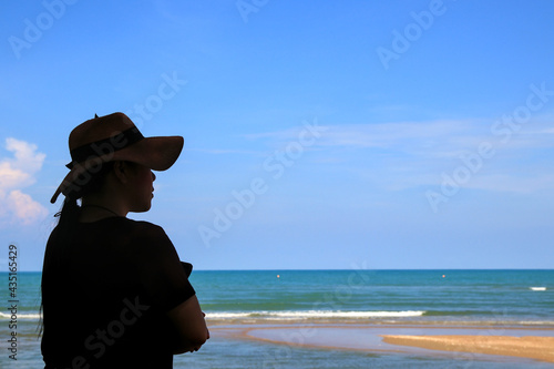 A woman in a wide-brimmed hat stands with her arms folded. Enjoy the nature of the sea and clear sky. © Suthep