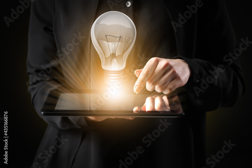 Businesswoman with tablet computer and glowing light bulb on dark background, closeup