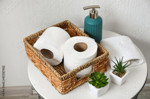 Basket with rolls of toilet paper, bottle of soap and houseplants on table in bathroom