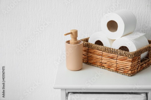 Basket with rolls of toilet paper and bottle of cosmetic product on table in bathroom