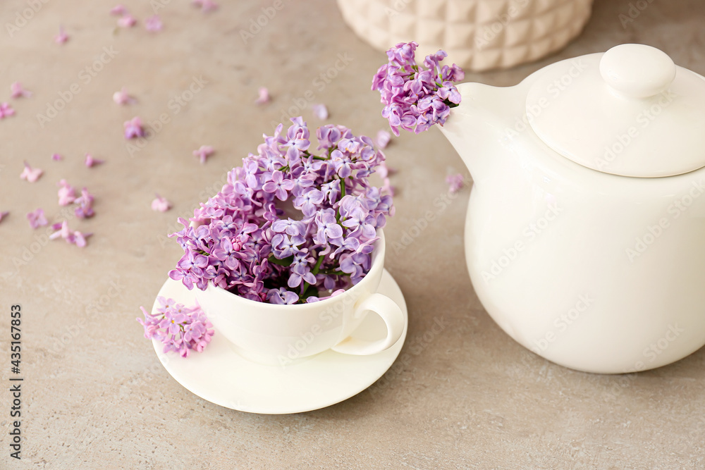 Cup with beautiful lilac flowers and teapot on light background Cup with beautiful lilac flowers and teapot on light background