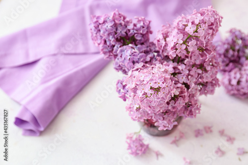 Glass with beautiful lilac flowers on light background