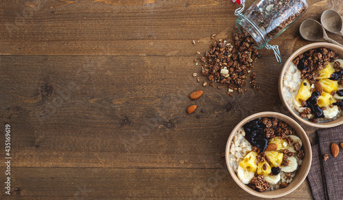 Oatmeal with pineapple, banana and chocolate granola in beige plates on a brown wooden table. A hearty healthy breakfast. A place for text.