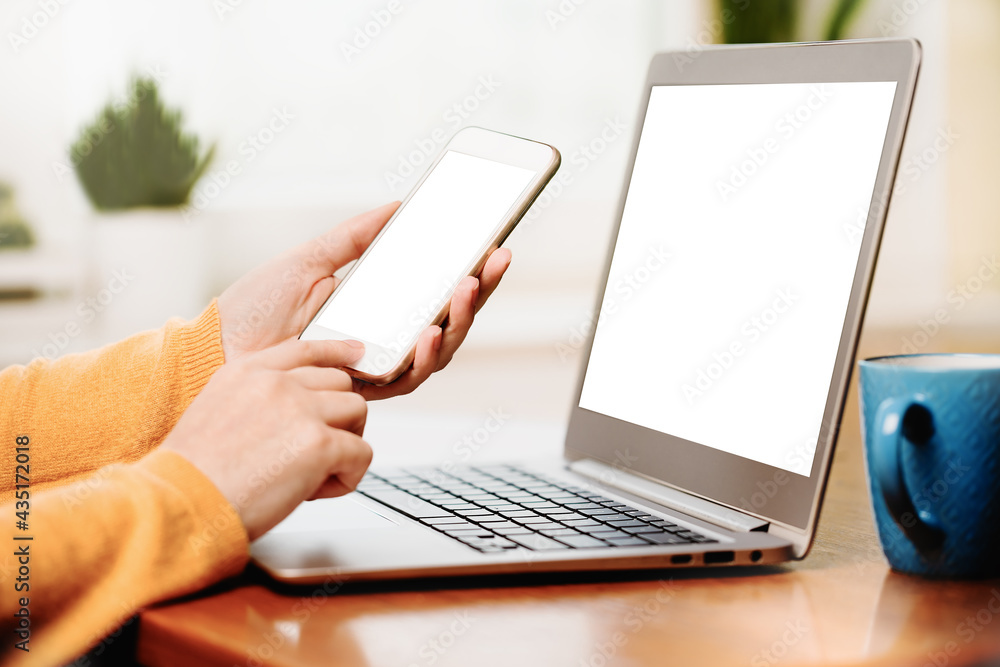 Close up banner of a woman using a mobile phone smartphone and laptop. Mockup white screens. Working at home or office desk. Online shopping banking or texting. Small business or social media Close up banner of a woman using a mobile phone smartphone and laptop. Mockup white screens. Working at home or office desk. Online shopping banking or texting. Small business or social media