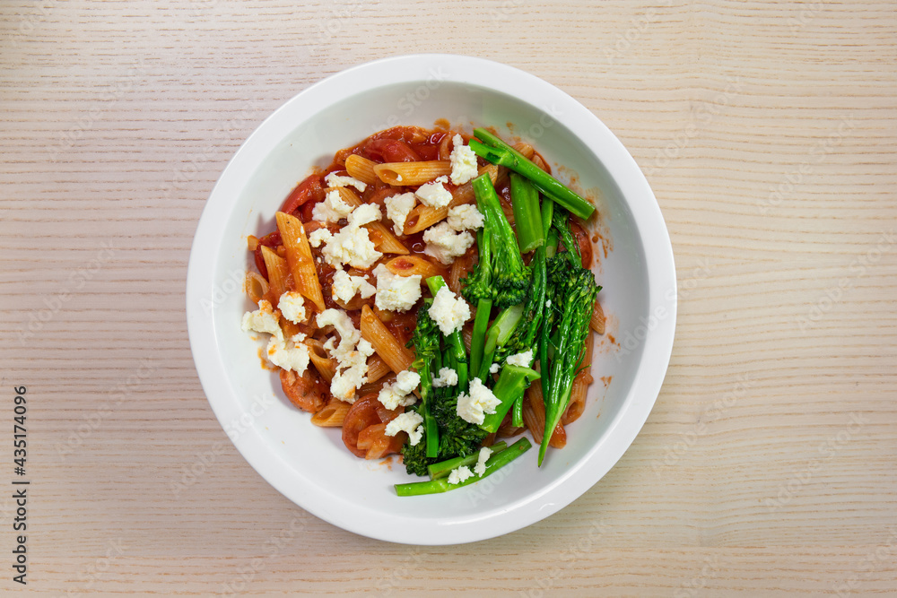 A bowl of tomato penne pasta with broccolini and feta cheese. A bowl of tomato penne pasta with broccolini and feta cheese.
