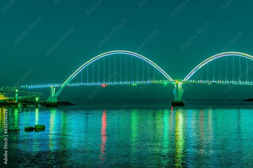 Fototapeta premium Night view of pedestrian bridge over ocean harbor lit up with beautiful lights.