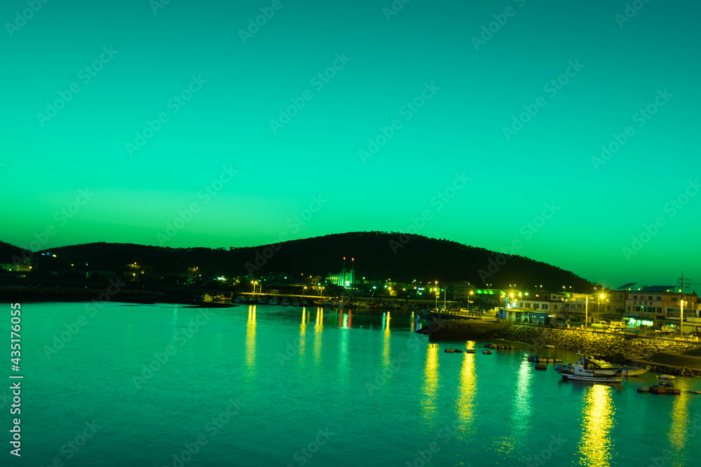 Fototapeta premium Night view of ocean fishing port with light reflecting off water.