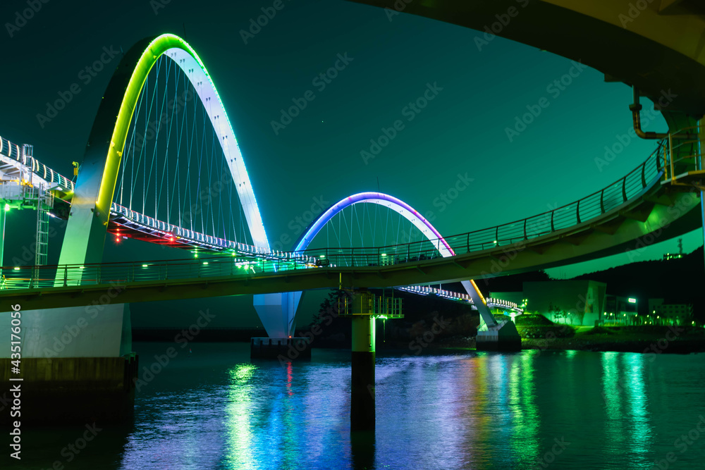 Obraz premium Night view of pedestrian bridge over ocean harbor lit up with beautiful lights.