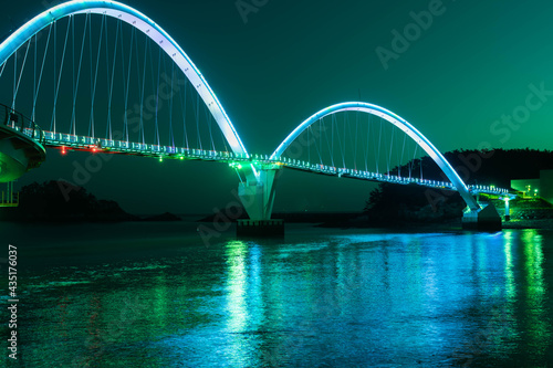 Fototapeta Naklejka Na Ścianę i Meble -  Night view of pedestrian bridge over ocean harbor lit up with beautiful lights.